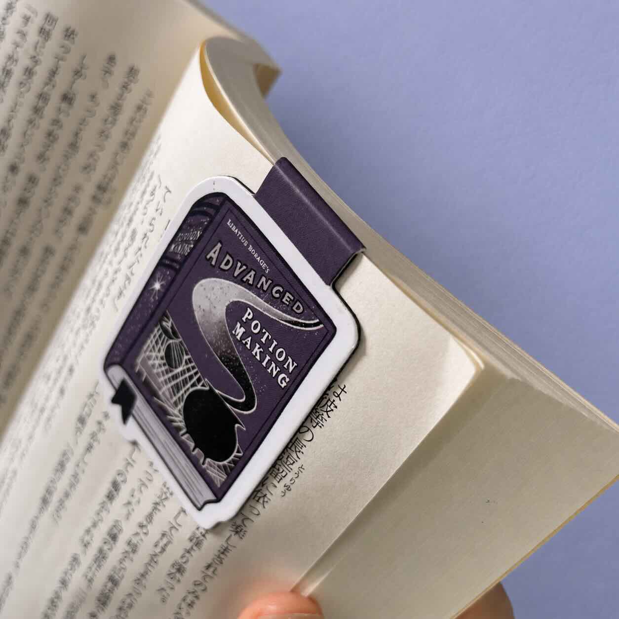 A purple and white book bookmark with 'Advanced Potion Making' printed on it, holding an open book against a light purple background.